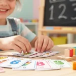 Dziecko układa kolorowe karty z działaniami matematycznymi i drewniane klocki na stole w klasie.