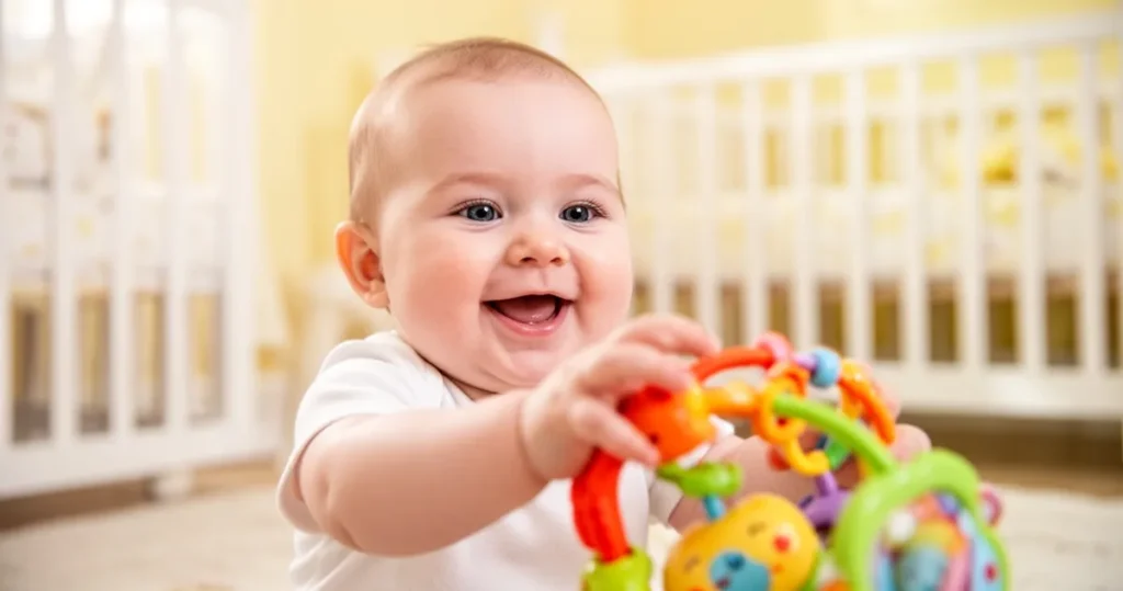 Uśmiechnięte 5-miesięczne dziecko sięgające po kolorową zabawkę w pokoju dziecka z miękkim oświetleniem.
