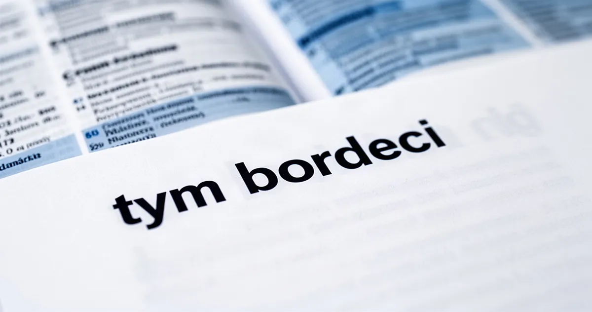 Zbliżenie na napis „tym bardziej” pogrubioną czcionką na białym papierze, w tle rozmyty słownik języka polskiego.